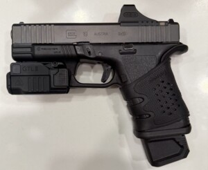 A black handgun with a grip and attachment sits on a white surface.