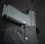 A handgun is secured in a black holster attached to a belt.