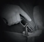 A person holding a handgun with a folding grip in a dark setting.