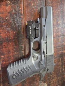 A gray handgun with a mounted flashlight on a wooden surface.