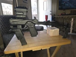 A modified handgun with a Vortex sight and folding brace on a wooden table in a living room.