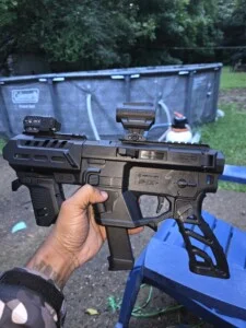 A person holding a black airsoft-style gun in a backyard setting.