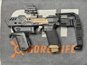 Customized handgun with attachments on a gray mat featuring orange and white text.